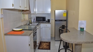 Cocina compacta con armarios blancos, microondas, refrigerador y una pequeña zona de comedor con mesa y sillas.