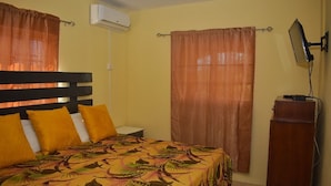 Una habitación con cama, aire acondicionado, escritorio, televisor y cortinas.