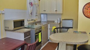 Cocina compacta con microondas, estufa y lavabo. Hay una mesa de comedor con sillas y un refrigerador pequeño.