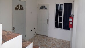 Un pasillo con puertas blancas, un extintor y una ventana con cortinas.