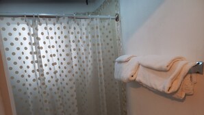 Un baño con cortina de ducha estampada con lunares, un toallero con toallas dobladas y una zona de ducha con azulejos.