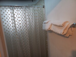 Ein Badezimmer mit Duschvorhang in Punkteoptik, einem Handtuchhalter mit gefalteten Handtüchern und einem gefliesten Duschbereich.