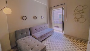 Habitación con sofá, un pequeño reposapiés y piso estampado. Se observan tres espejos montados en la pared y una lámpara.