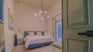 Un dormitorio con cama, mesitas de noche, lámpara colgante, ventana con cortinas y una puerta.