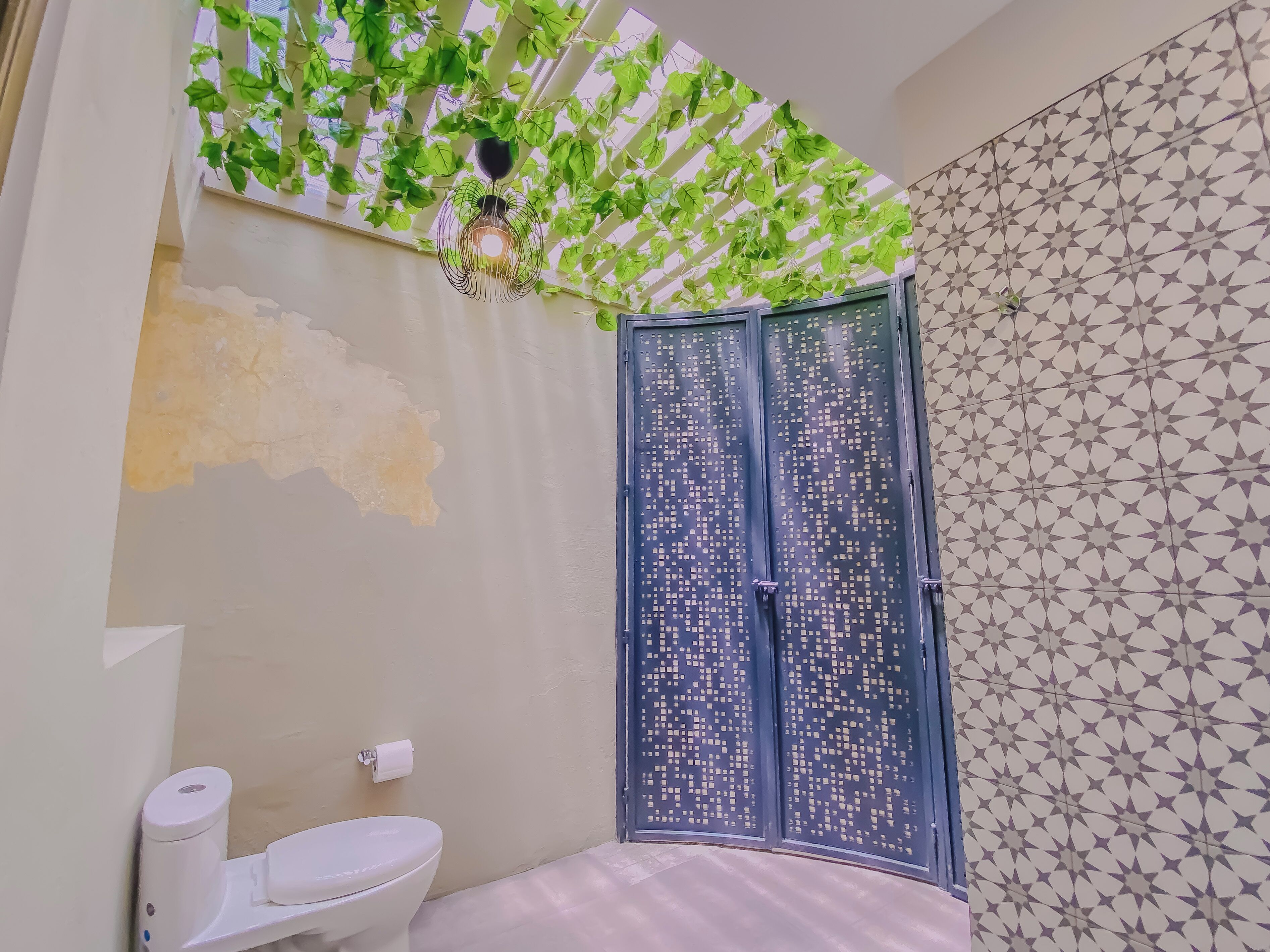 Baño con inodoro, secador de manos, dispensador de toallas y ducha con puerta de diseño geométrico.