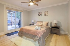 Ein Schlafzimmer mit einem Bett, zwei Nachttischen mit Lampen, einem Deckenventilator, einer Schiebeglastür zu einem Außenbereich und zwei Wandbildern mit Blumenmotiven.