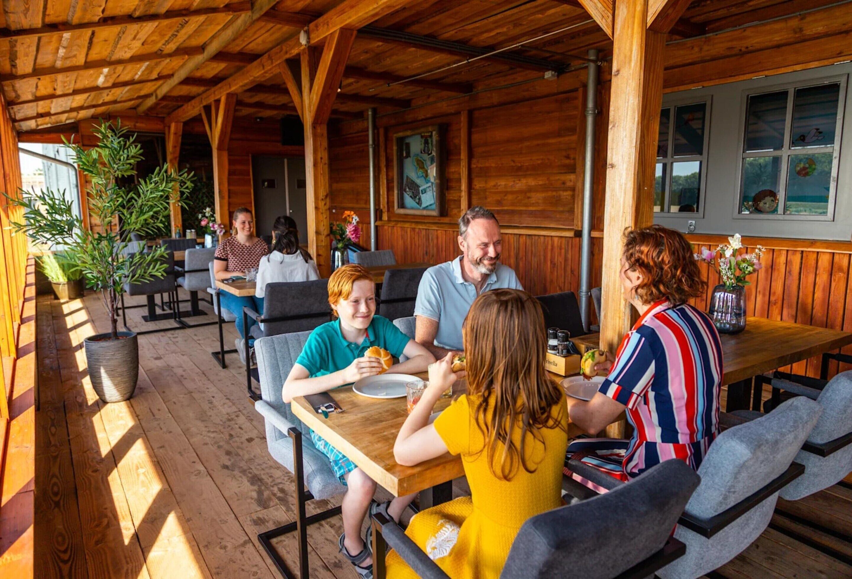 Une cabane en bois dotée d’un espace repas couvert, de tables et de chaises.