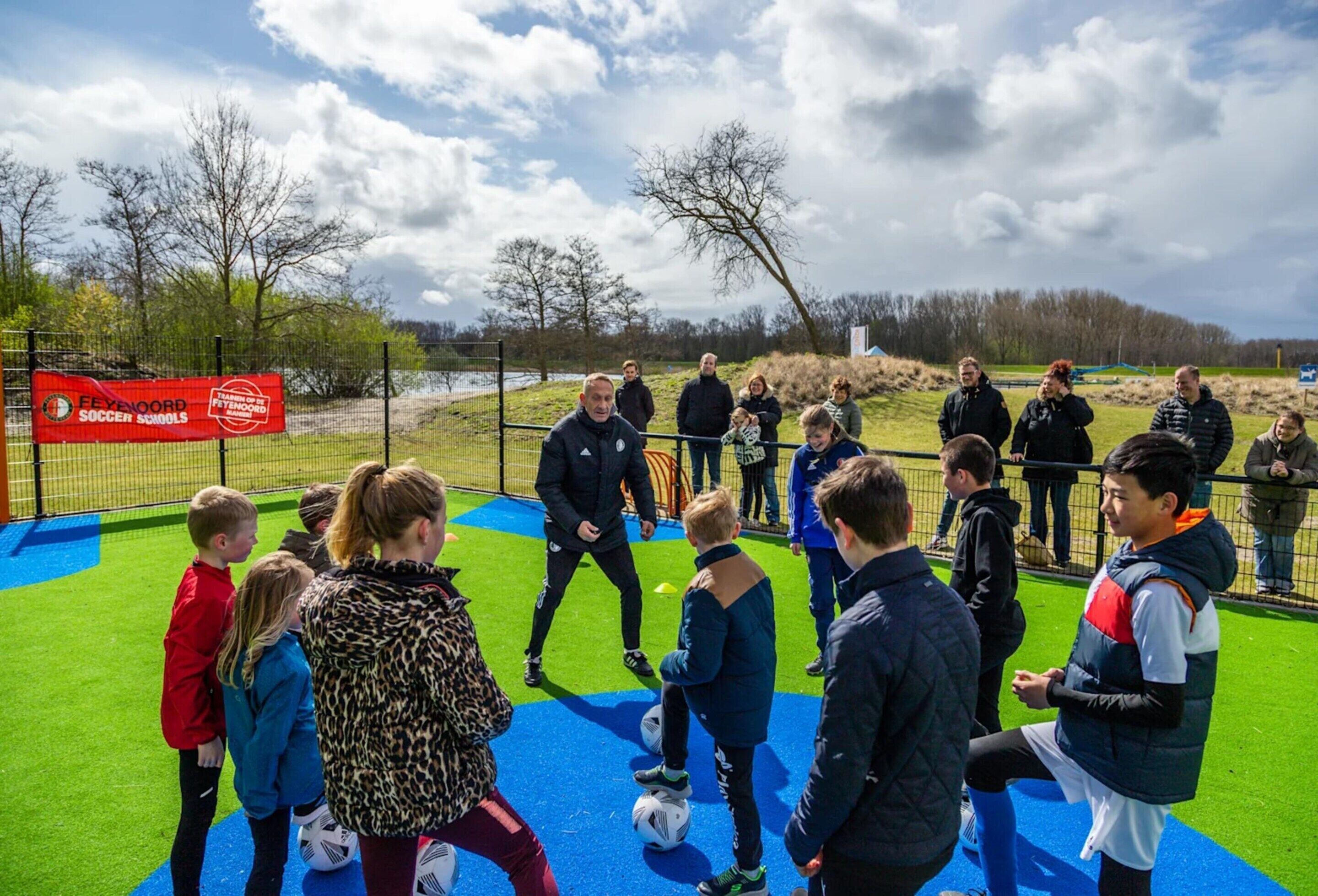 A group of people on a soccer field with a banner reading "Feyenoord Soccer Schools".