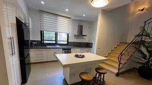 Eine moderne Küche mit einer zentralen Kochinsel, Holzstühlen, einer Treppe und einem Blumentopf.