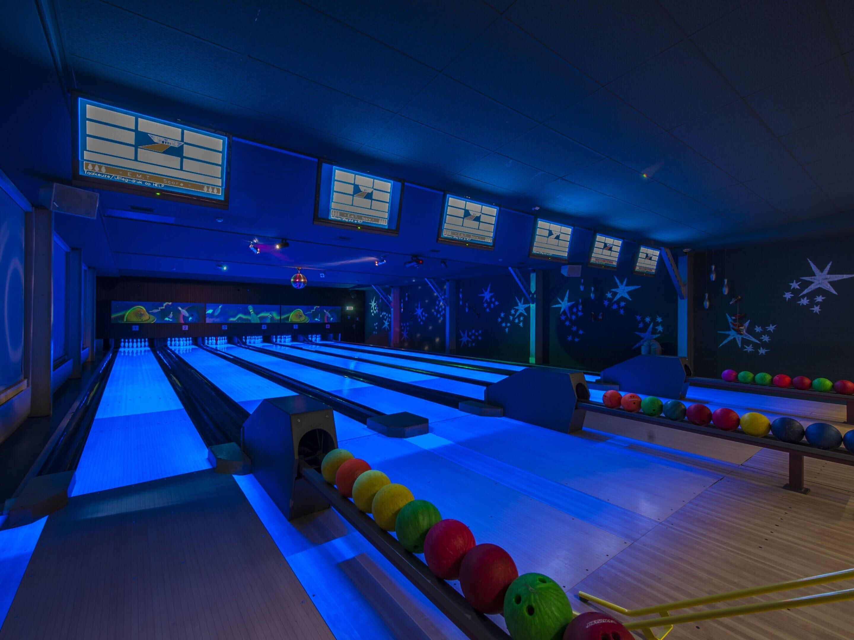A bowling alley with multiple lanes, colorful bowling balls, and a scoreboard.