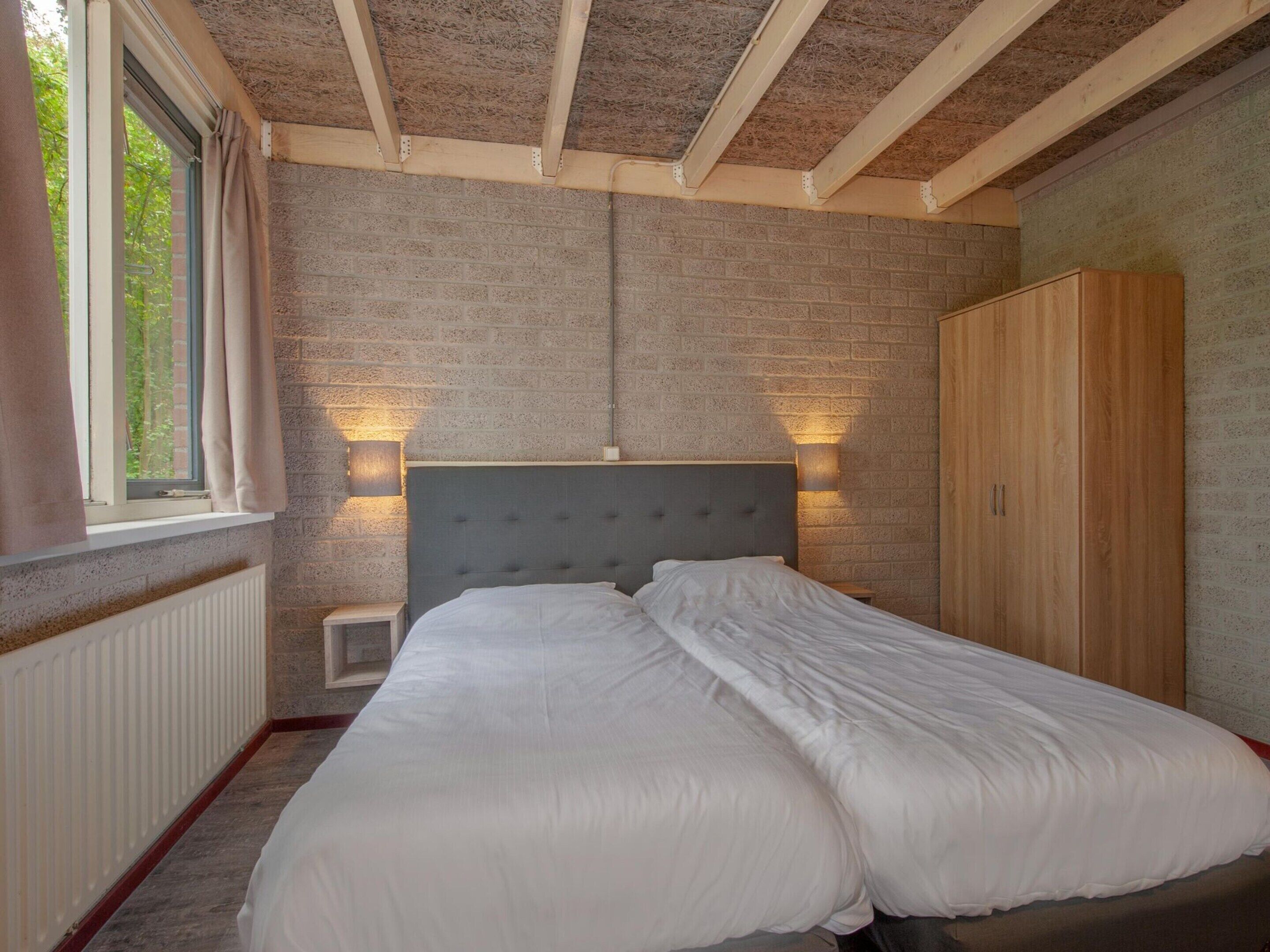 A bedroom with a bed, a wardrobe, a window with curtains, and a brick wall.