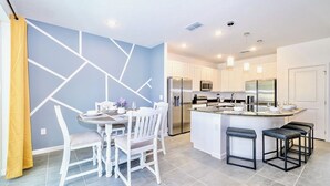 A modern kitchen with white cabinetry, a central island with bar stools, and a dining area with a round table and chairs.