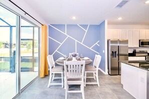 Una cocina moderna con armarios blancos, electrodomésticos de acero inoxidable y una zona de comedor con una pared de acento azul y sillas blancas.