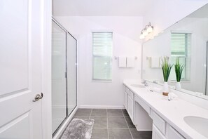 Un baño moderno con ducha de vidrio, tocador blanco y un espejo grande.