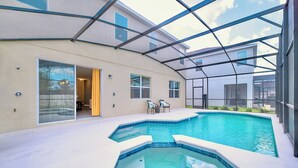 A covered outdoor swimming pool with a hot tub, surrounded by a glass enclosure, and a patio area with chairs.