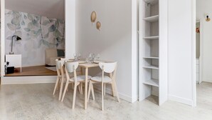 Un comedor moderno con una mesa y sillas de madera, una pared blanca con un diseño de hojas y un armario blanco con estantes.