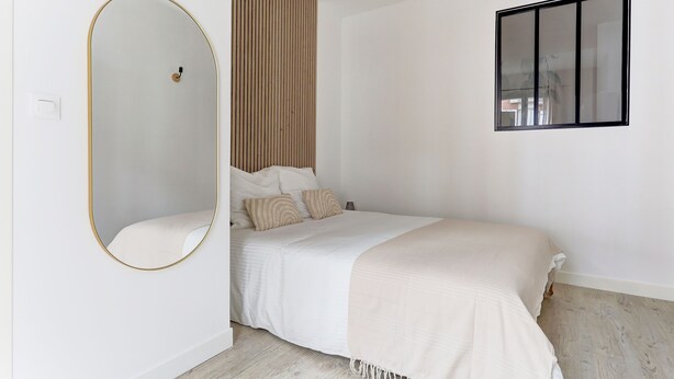Un dormitorio con cama, espejo, ventana y pared de paneles de madera.
