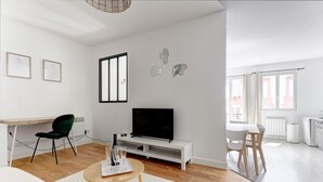 Una sala de estar moderna con un televisor de pantalla plana, una mesa de comedor y un espacio de trabajo con escritorio y silla.