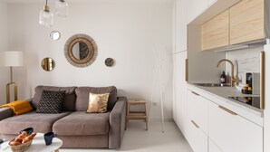 A modern living room with a sofa, coffee table, and a small wooden stool. There is a kitchen area with white cabinets and a sink. - Ty Peskaiden 1 -  à Cancale, vue mer (Cancale)