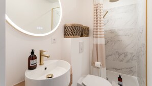 A bathroom with a round mirror, a sink, a toilet, and a shower area. - Ty Peskaiden 1 -  à Cancale, vue mer (Cancale)