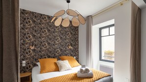 A modern hotel room with a patterned wallpaper, a large bed with a yellow blanket, and a view of the outdoors through a window. - Ty Peskaiden 1 -  à Cancale, vue mer (Cancale)