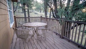 A wooden deck with a metal table and chairs, surrounded by a wooden railing. - Cozy 2-bedroom cabin in lovely Ruidoso (Ruidoso)