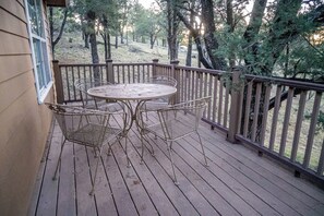 Un terrazzo in legno con tavolo e sedie in metallo, circondato da una ringhiera in legno.