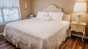 A neatly made bed with a white bedspread and pillows, a bedside lamp, and a nightstand with books. - Cozy 2-bedroom cabin in lovely Ruidoso (Ruidoso)