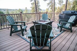 A wooden deck with Adirondack chairs, a table with a fire pit, and a grill.
