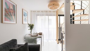 En moderne stue med en sofa, et spisebord med stole, en trappe og billeder i rammer på væggene.