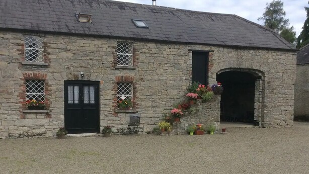A stone building with a black door, multiple windows, and a gravel driveway. - The Coach house of Durhamstown Castle

 (Bohermeen)