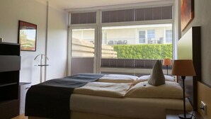 Une chambre d’hôtel avec un lit, un bureau, une lampe et une fenêtre avec des stores.