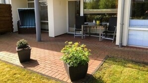 Un espace patio aménagé avec une table et des chaises, un petit coin salon et deux plantes en pot.