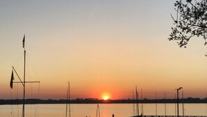 Un port de plaisance avec des bateaux amarrés, une jetée s’avançant dans l’eau et un coucher de soleil en arrière-plan.
