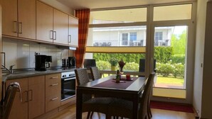 Une cuisine moderne avec des meubles en bois, une table à manger avec des chaises et une grande fenêtre donnant sur un balcon et la verdure.