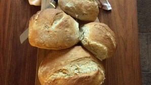 A wooden table with four loaves of bread on a cutting board.
