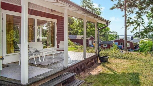 A wooden deck with white chairs and a table, overlooking a grassy area with a lake and houses in the background. - Pet friendly home in Mariefred with WiFi (Mariefred)