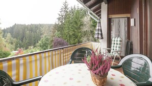 A balcony with a table and chairs, a potted plant, and a view of a forested area. - Ferienwohnung mit Balkon im Schwarzwald (Waldachtal)