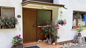 A house with a wooden door, a small porch with a mat, and potted plants. - Ferienwohnung mit Balkon im Schwarzwald (Waldachtal)