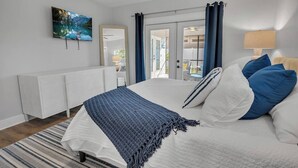 Un dormitorio con cama, televisor, ventana con cortinas, mesita de noche y vistas al exterior.