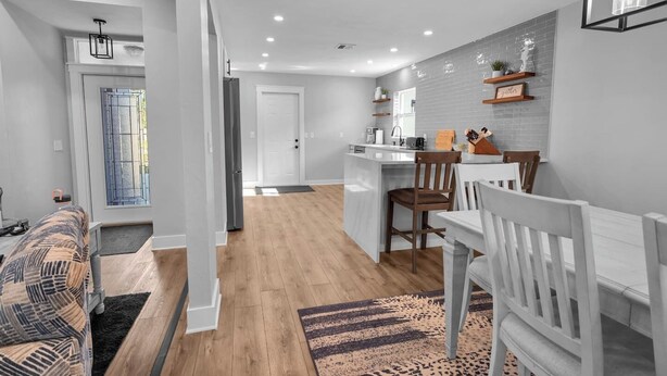 Una cocina moderna con una isla central, piso de madera y un comedor con sillas blancas.