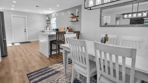 Una cocina moderna con una isla central, armarios blancos y un comedor con sillas blancas.