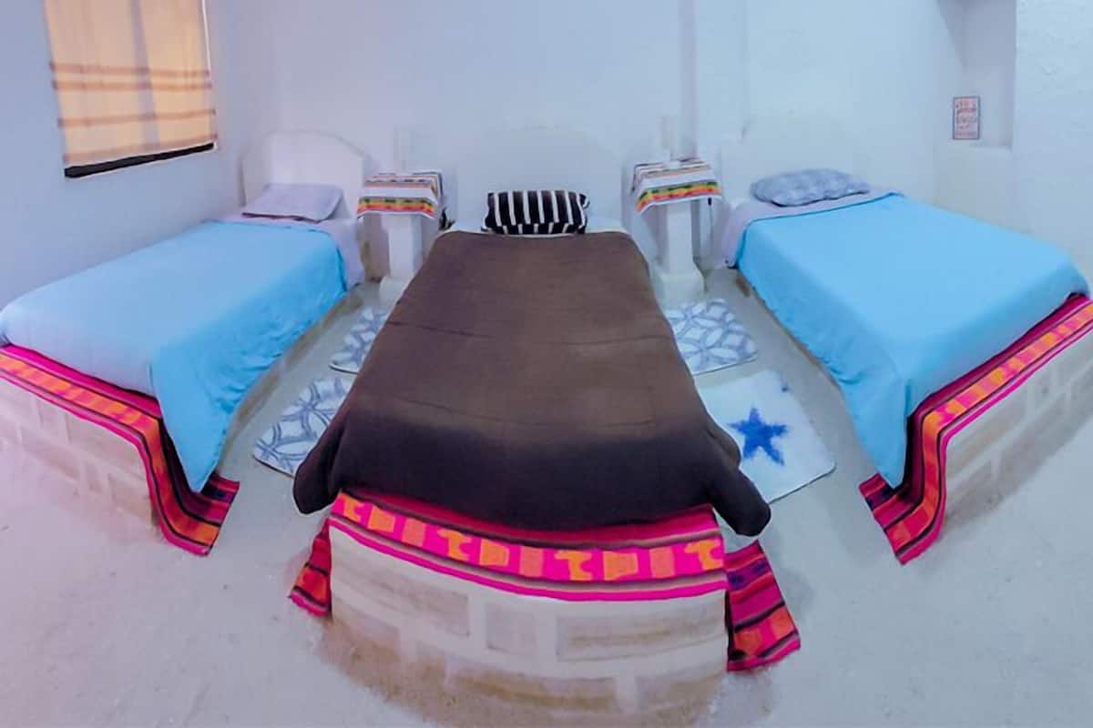 Una habitación con dos camas, un banco y una mesita.