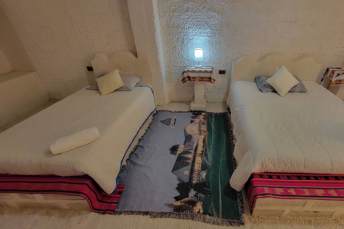 Una habitación con dos camas, una mesita con lámpara y un tapete estampado.