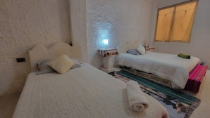 A cozy bedroom with two beds, a small table, and a window with curtains. - hostal beds of salt ga (Uyuni)