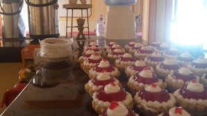 A buffet table with a variety of desserts, including cupcakes with cream and red toppings, and a water dispenser in the background. - hostal beds of salt ga (Uyuni)