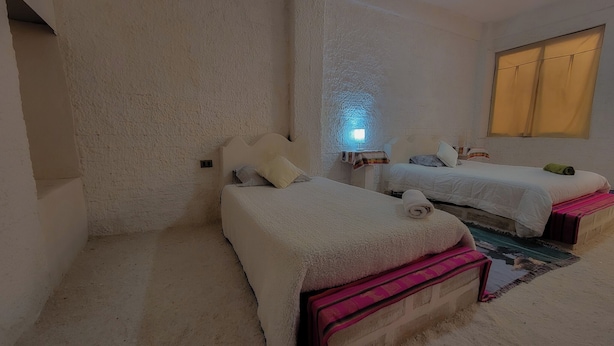 A room with two beds, a small table, and a window with curtains. - hostal beds of salt ga (Uyuni)