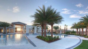 Zona de piscina con palmeras, un área de estar techada y un edificio con amplias ventanas.