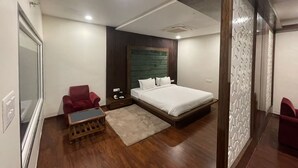 A modern hotel room with a large bed, a wooden floor, a red armchair, a small wooden table, and a decorative wall panel. - Mann Holiday Resort (Burhanpur)