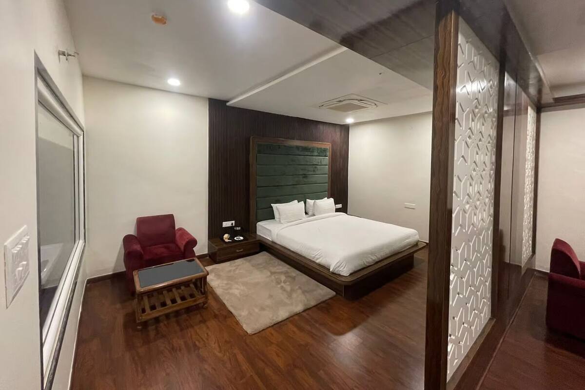 A modern hotel room with a large bed, a wooden floor, a red armchair, a small wooden table, and a decorative wall panel.